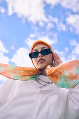 Image showing Portrait, fashion or hijab with a saudi woman outdoor on a blue sky background in a scarf and sunglasses for style. Muslim, faith or religion with a trendy young arab person outside in modern clothes