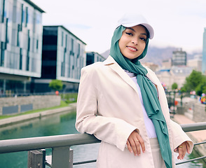 Image showing Portrait, fashion or religion with a happy muslim woman in th city wearing a cap and scarf for urban style. Islam, faith or hijab with a trendy young arab person smiling outside in modern clothes