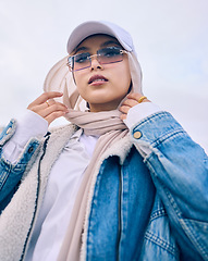 Image showing Portrait, fashion or low angle with a muslim woman outdoor in a cap, sunglasses and scarf for contemporary style. Islam, faith or hijab with a trendy young arab person posing alone in modern eyewear