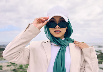 Image showing Portrait, fashion or sunglasses with a saudi woman outdoor in a cap and scarf for contemporary style. Islam, face and hijab with a trendy young muslim or arab person posing outside in modern clothes