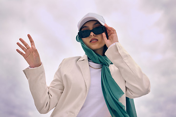 Image showing Portrait, fashion or religion with a muslim woman on a cloudy sky background in a cap and scarf for modern style. Islam, faith or hijab with a trendy young arab person outside in contemporary clothes