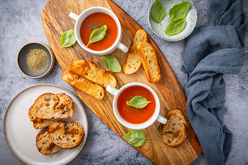 Image showing Homemade tomato soup with basil, toast and olive oil on a wooden cutting board. 