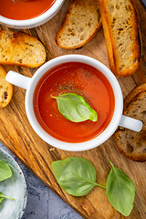 Image showing Homemade tomato soup with basil, toast and olive oil on a wooden