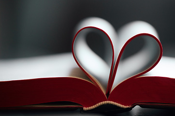 Image showing Book, pages and fold with heart shape in closeup for reading, learning or literature by blurred background. Paper, icon and love story with emoji for education, knowledge and development at library