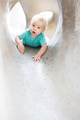 Image showing Child playing on outdoor playground. Toddler plays on school or kindergarten yard. Active kid on stone sculpured slide. Healthy summer activity for children. Little boy climbing outdoors.