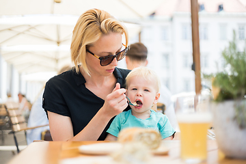 Image showing Young mother relaxing together with her little child, adorable toddler girl, in summer outdoors cafe drinking coffee and eating muffin or cupcke. Family in love. Kid an beautiful woman.