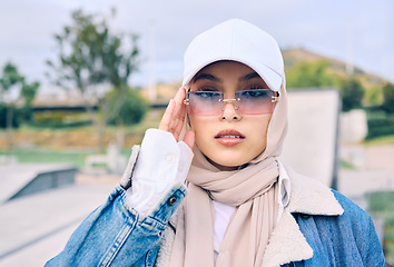 Image showing Portrait, fashion or sunglasses with an islamic woman outdoor in a cap and scarf for contemporary style. Muslim, faith or hijab with a trendy young arab female person posing outside in modern eyewear