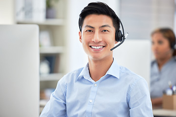 Image showing Portrait of asian call centre agent talking on headset while working on computer in office. Confident and smiling businessman consulting and operating a helpdesk for customer sales and service suppor