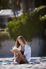 Image showing Woman on the beach, reading book and travel, relax in nature in summer holiday with peace and calm. Young female person is outdoor with novel to read, seaside vacation and relaxation in the sun