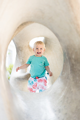 Image showing Child playing on outdoor playground. Toddler plays on school or kindergarten yard. Active kid on stone sculpured slide. Healthy summer activity for children. Little boy climbing outdoors.