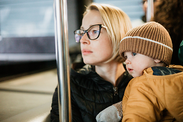 Image showing Mother carries her child while standing and holding on to the bus. Mom holding her infant baby boy in her arms while riding in a public transportation. Cute toddler boy traveling with his mother.