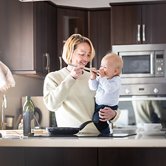 Image showing Happy mother and little infant baby boy cooking and tasting healthy dinner in domestic kitchen. Family, lifestyle, domestic life, food, healthy eating and people concept.