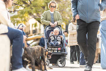 Image showing Mother walking and pushing his infant baby boy child in stroller in crowd of people wisiting sunday flea market in Malaga, Spain.