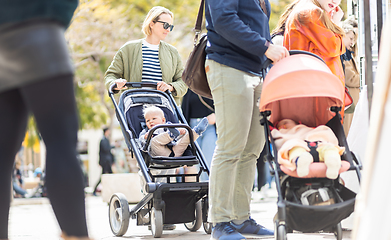 Image showing Mother walking and pushing his infant baby boy child in stroller in crowd of people wisiting sunday flea market in Malaga, Spain.