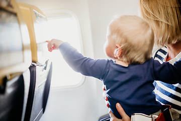 Image showing Mom and child flying by plane. Mother holding and playing with her infant baby boy child in her lap during economy comercial flight. Concept photo of air travel with baby. Real people.