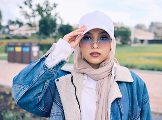 Image showing Portrait, fashion or eyewear with a muslim woman outdoor in a cap and scarf for contemporary style. Islam, faith and hijab with a trendy young arab female person posing outside in modern sunglasses