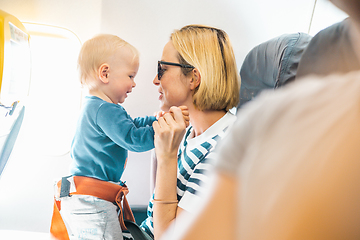 Image showing Mom and child flying by plane. Mother holding and playing with her infant baby boy child in her lap during economy comercial flight. Concept photo of air travel with baby. Real people.