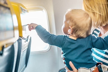 Image showing Mom and child flying by plane. Mother holding and playing with her infant baby boy child in her lap during economy comercial flight. Concept photo of air travel with baby. Real people.