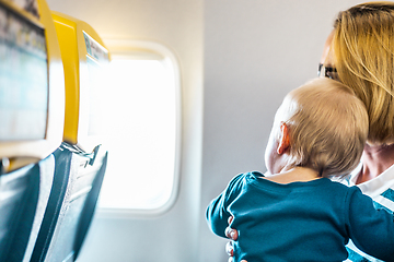 Image showing Mom and child flying by plane. Mother holding and playing with her infant baby boy child in her lap during economy comercial flight. Concept photo of air travel with baby. Real people.