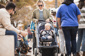 Image showing Mother walking and pushing his infant baby boy child in stroller in crowd of people wisiting sunday flea market in Malaga, Spain.