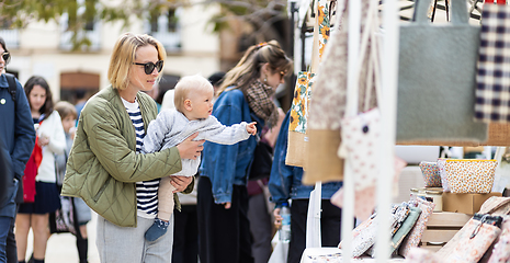 Image showing Mother walking carrying his infant baby boy child in crowd of people wisiting sunday flea market in Malaga, Spain