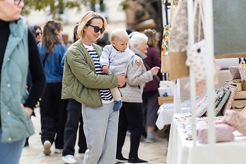 Image showing Mother walking carrying his infant baby boy child in crowd of people wisiting sunday flea market in Malaga, Spain