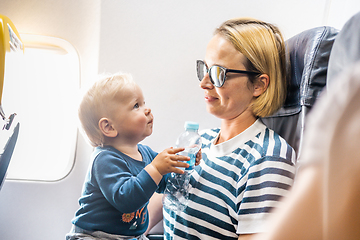 Image showing Mom and child flying by plane. Mother holding and playing with her infant baby boy child in her lap during economy comercial flight. Concept photo of air travel with baby. Real people.