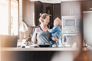 Image showing Happy mother and little infant baby boy together making pancakes for breakfast in domestic kitchen. Family, lifestyle, domestic life, food, healthy eating and people concept.