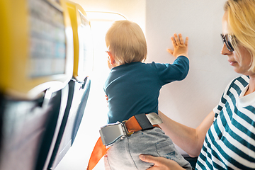 Image showing Mom and child flying by plane. Mother holding and playing with her infant baby boy child in her lap during economy comercial flight. Concept photo of air travel with baby. Real people.