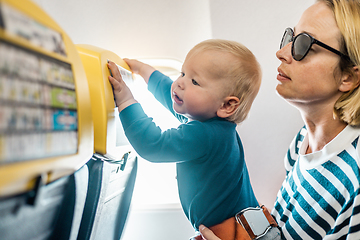 Image showing Mom and child flying by plane. Mother holding and playing with her infant baby boy child in her lap during economy comercial flight. Concept photo of air travel with baby. Real people.