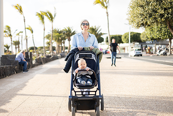 Image showing Young mother walking and pushing her infant boy child in baby stroller along palm lined beach promenade of Puerto del Carmen, Lanzarote, Canary islands, Spain