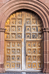 Image showing Big beautiful ornate wooden door, framed by a decorated stone arch. Entrance to iglesia de nuestra senora de guadalupe, Teguise, Lanzarote, Canary Islands, Spain.