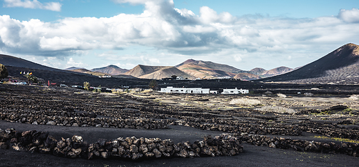 Image showing Traditional white houses in black volcanic landscape of La Geria wine growing region with view of Timanfaya National Park in Lanzarote. Touristic attraction in Lanzarote island, Canary Islands, Spain.