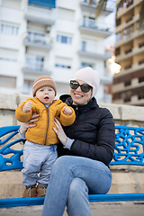 Image showing Young mother with her cute infant baby boy child on bench in city park.