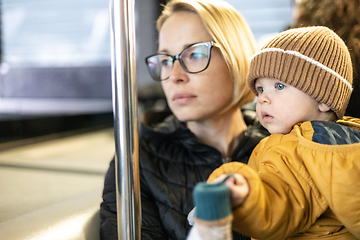 Image showing Mother carries her child while standing and holding on to the bus. Mom holding her infant baby boy in her arms while riding in a public transportation. Cute toddler boy traveling with his mother.