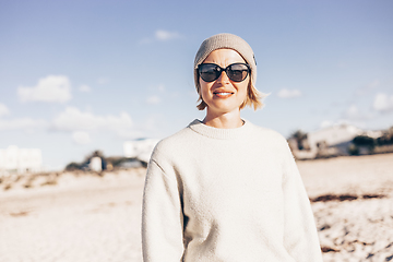 Image showing Portrait of young stylish woman wearing wool sweater, wool cap and sunglasses on long sandy beach in spring