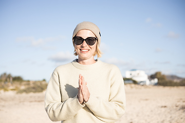 Image showing Portrait of young stylish woman wearing wool sweater, wool cap and sunglasses on long sandy beach in spring