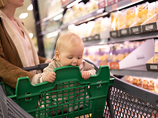 Image showing Caucasian mother shopping with her infant baby boy child choosing products in department of supermarket grocery store.