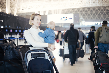 Image showing Motherat travelling with his infant baby boy child, walking, pushing baby stroller and luggage cart at airport terminal station. Travel with child concept.