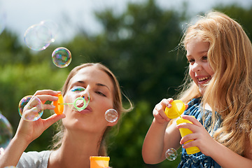 Image showing Mother blowing bubbles with daughter, happiness outdoor with bonding and love with childhood and parenting. Woman playing outside with young girl, mom and female child with fun activity together