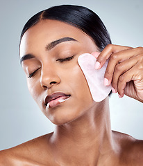 Image showing Beauty, facial and gua sha with face of woman in studio for massage, wellness and cosmetics. Spa, self care and glow with model on grey background for skincare, cosmetology and rose quartz crystal