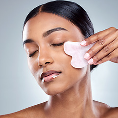 Image showing Massage, skincare and gua sha with face of woman in studio for beauty, wellness and cosmetics. Spa, self care and glow with model on grey background for facial, cosmetology and rose quartz crystal