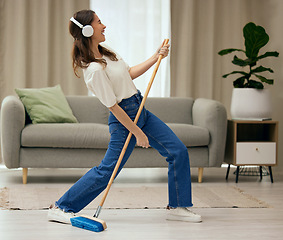 Image showing Woman, singer and broom to clean living room with funny dance, sweeping floor and rock performance in home. Girl, comic singing and cleaner with spring cleaning, music and headphones for guitar solo