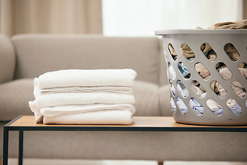Image showing Clean laundry, table and basket in home living room for folding, hospitality and housekeeping. Towel stack, plastic bucket and spring cleaning service for fabric, clothes and hygiene on desk in house