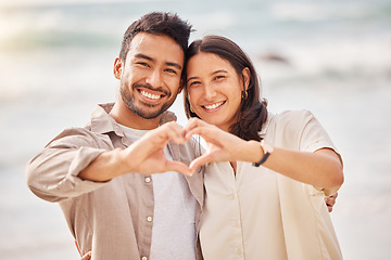 Image showing She completes me. Couple, portrait and love sign with hands at the ocean for travel with sunshine with a smile. Beach, together and heart with hand and smile in the summer for a weekend with romance.