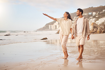 Image showing Mockup, pointing and a couple holding hands on the beach while walking together on a date for romance. Love, happy or smile with a man and woman taking a romantic walk by the coastal ocean or sea