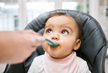 Image showing Adorable, sweet and cute baby eating puree for lunch, dinner or snack in her high chair at home. Child development, food and girl infant kid enjoying meal with spoon for growth and wellness in house.