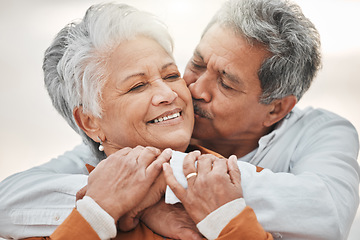 Image showing Happy elderly couple, hug and sunset with kiss on cheek, bonding and smile for romance, love and vacation. Senior man, woman and embrace with happiness, retirement and travel together for holiday