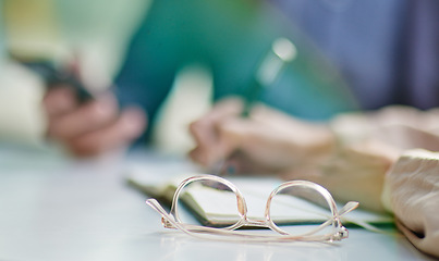 Image showing Glasses on desk, vision and eye care with business people in meeting, writing in notebook with strategy collaboration closeup. Eyewear, prescription lens and notes with ideas, planning with team