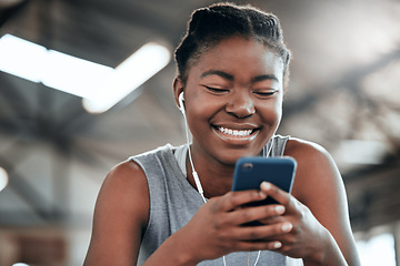 Image showing Phone, earphones and happy black woman in gym for fitness, sports or exercise. Smartphone, music and African female athlete on social media break, internet and web texting after workout or training.